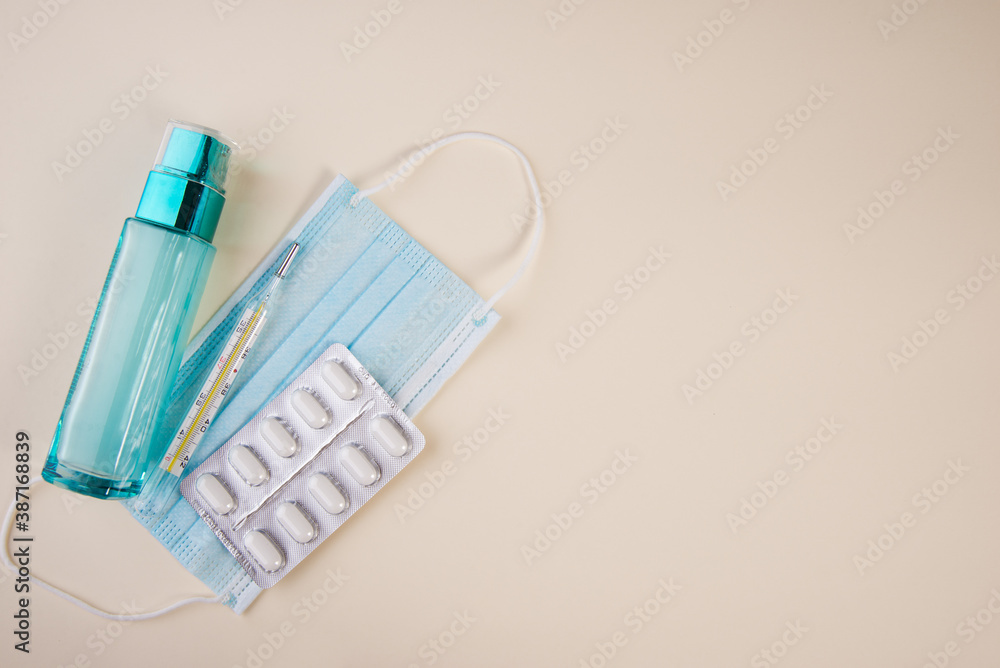 Protective medical mask with antibacterial gel and tablets with a thermometer on yellow background. Copy space. Protective medical mask with antibacterial gel and tablets with a thermometer on yellow background. Copy space.