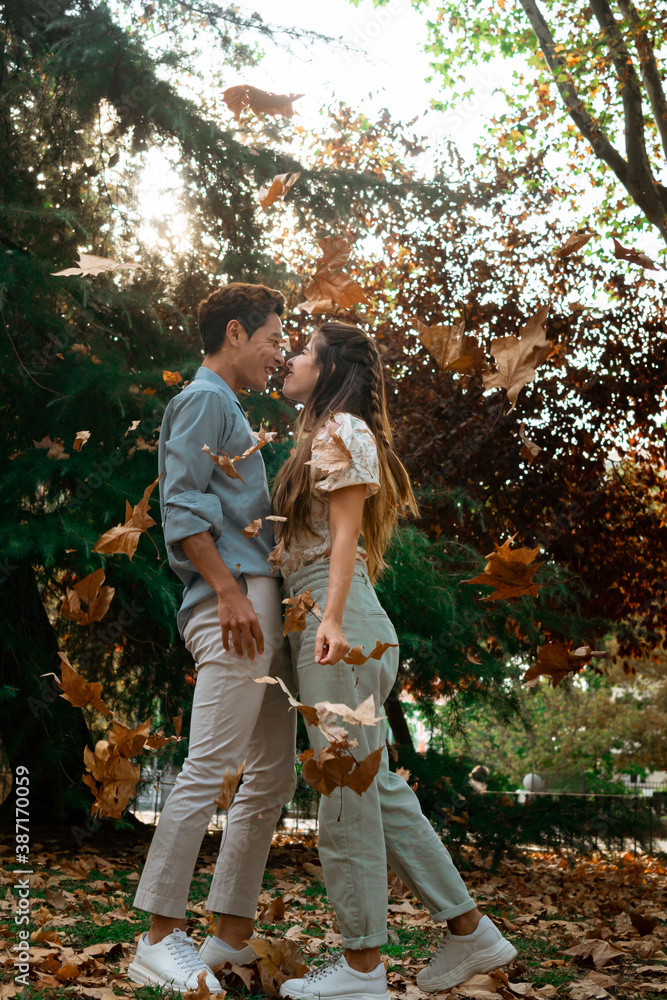 Interracial korean and spanish couple kissing in the park while leafs are falling beside them