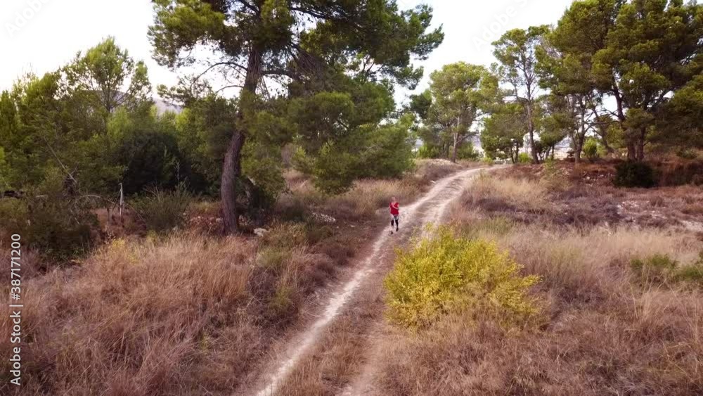 Young woman in red and black skin-tight sportswear runs along the road in the woods. Young woman in red and black skin-tight sportswear runs along the road in the woods.