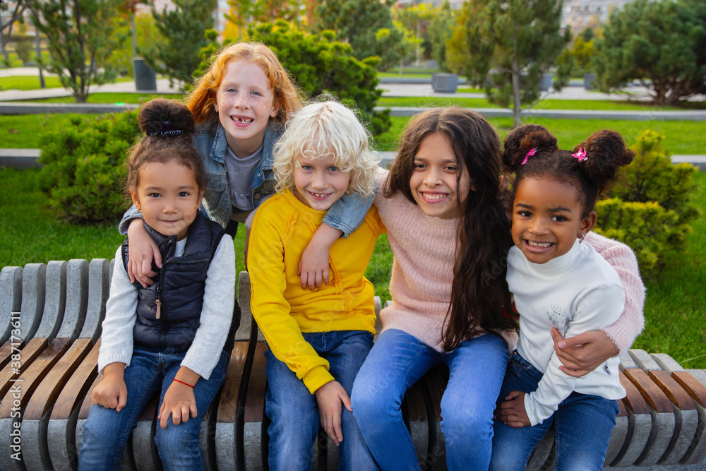 Fototapeta premium Warm. Interracial group of kids, girls and boys playing together at the park in summer day. Friendship has no race. Happiness, childhood, education, diversity concept. Look happy and sincere.