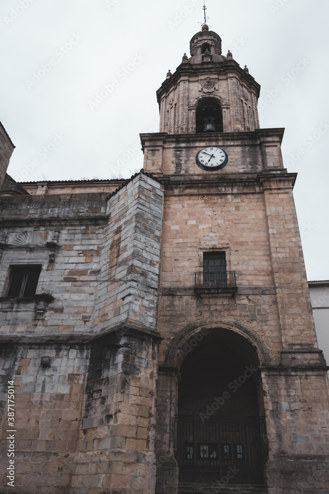 Medieval church with clock and bell in Portugalete, Spain. Religious architecture. Ancient cathedral tower with outdoor clock on facade. Elegant catholic church. Old stone church. with closed entrance