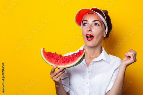 Young woman in red visor holding a slice of watermelon on yellow background.