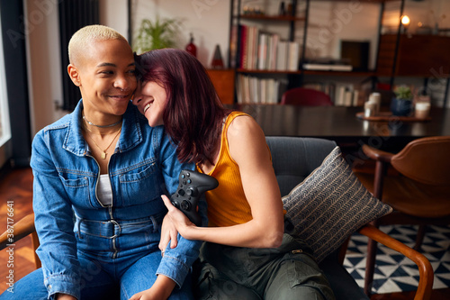 Loving Same Sex Female Couple Sitting On Sofa At Home Gaming Together