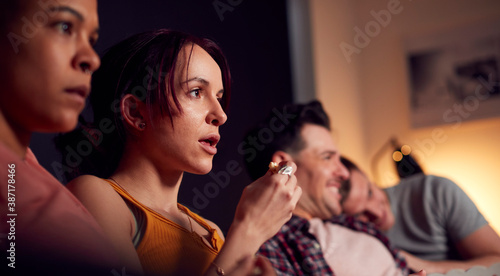 Group Of Gay Friends Sitting On Sofa At Home Watching Horror Movie On TV Together