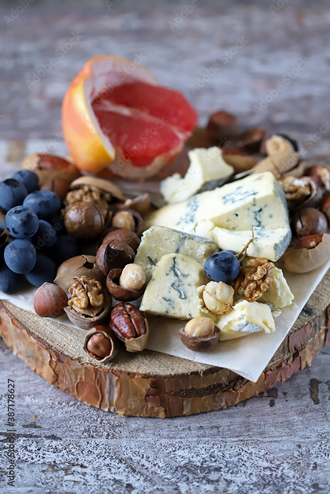 Fototapeta premium Selective focus. Cheese, nuts and fruits. Cheese snack on a wooden stand. Wine appetizer.