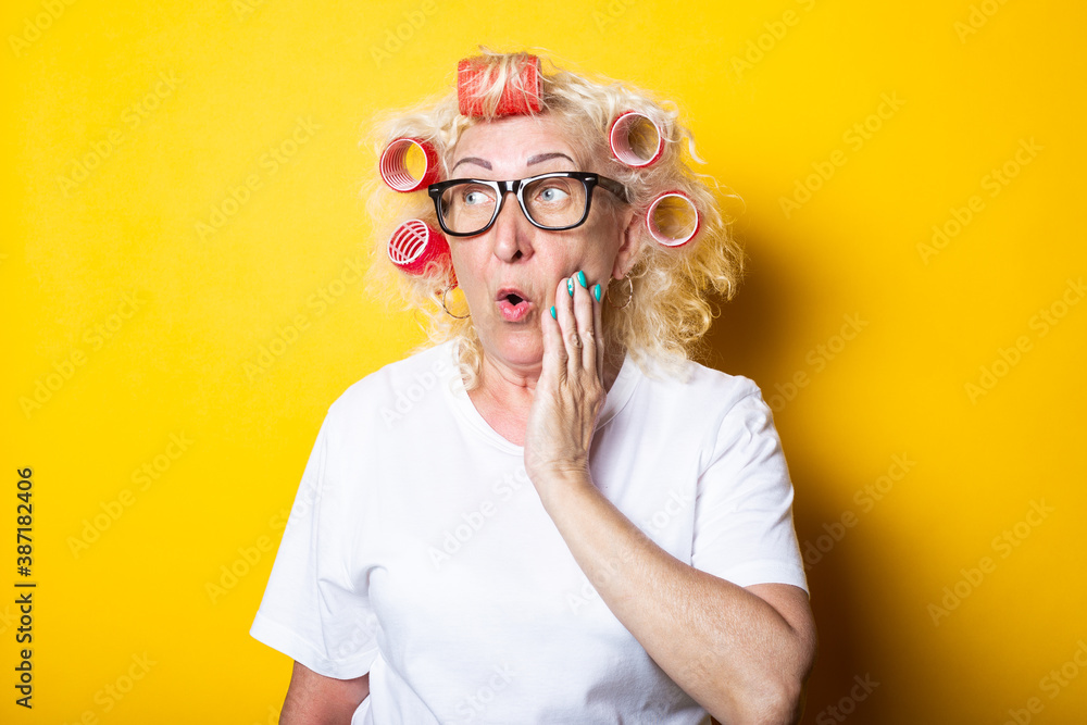 Surprised shock old woman with curlers in a white t-shirt on a yellow background Surprised shock old woman with curlers in a white t-shirt on a yellow background