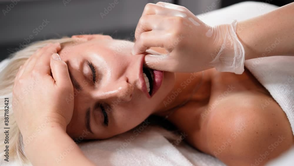 Woman masseur makes face relaxing massage and oral cavity to young beautiful female client blonde. Spa treatment for perfect skin in beauty salon. Cosmetology services. Healthcare and medicine Woman masseur makes face relaxing massage and oral cavity to young beautiful female client blonde. Spa treatment for perfect skin in beauty salon. Cosmetology services. Healthcare and medicine