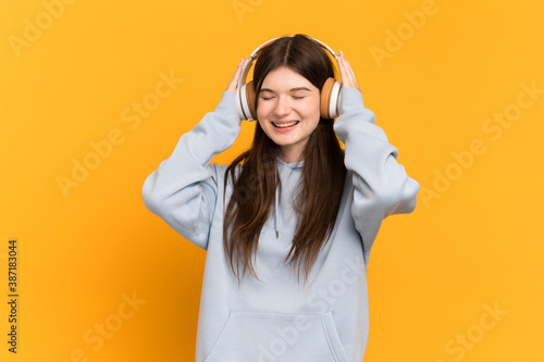 Young Ukrainian girl isolated on yellow background listening music