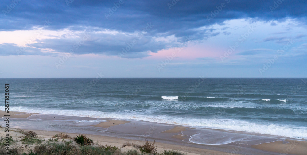 sand dunes and waves breaking on an endless beach under a stormy sky at sunrise