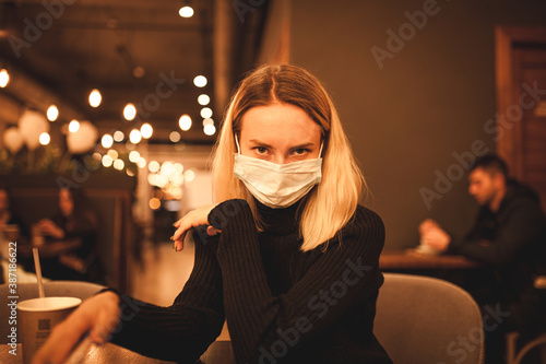Young woman is sitting in a cafe. Blond woman in mask. Quarantine time. 