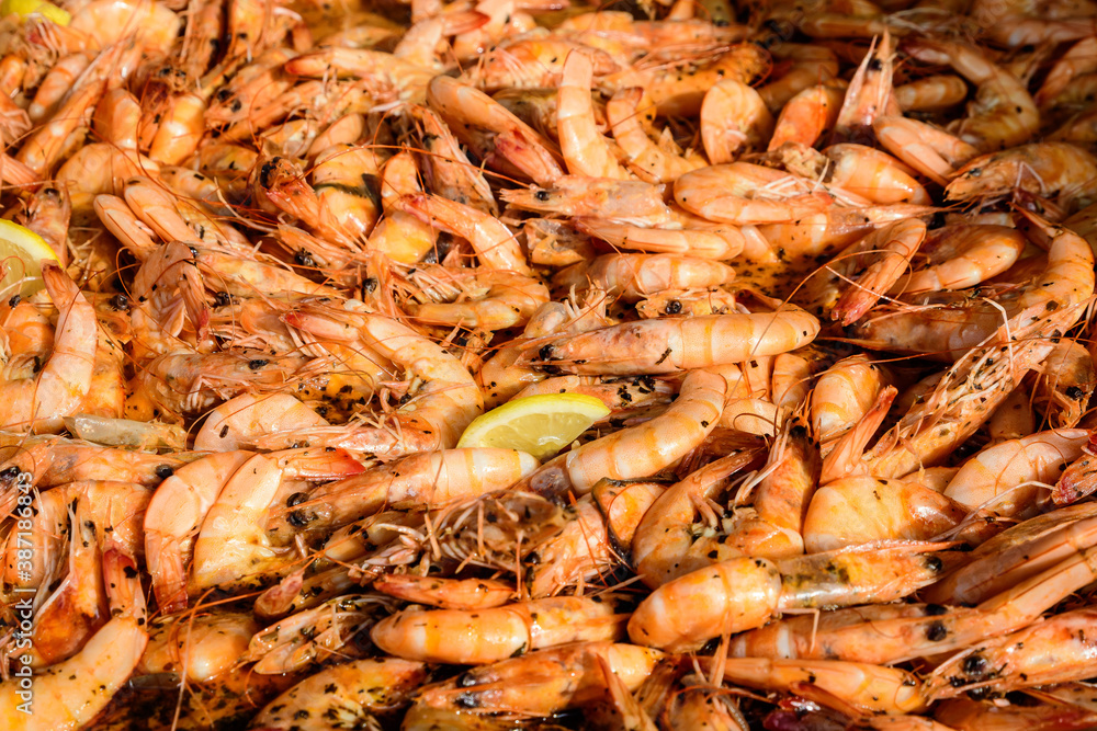 Close up of large portion of cooked shrimps with tomato sauce and yellow lemons in a large pan at a street food festival, ready to eat healthy seafood, beautiful orange monochrome outdoor background. Close up of large portion of cooked shrimps with tomato sauce and yellow lemons in a large pan at a street food festival, ready to eat healthy seafood, beautiful orange monochrome outdoor background.
