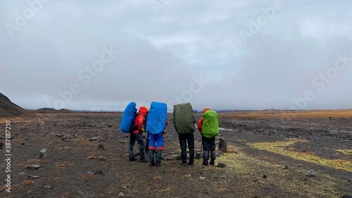 Group of tourists with large backpacks and trekking poles stand in a semicircle.