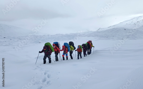 A group of climbers with backpacks and trekking poles are walking along a snow-covered trail.