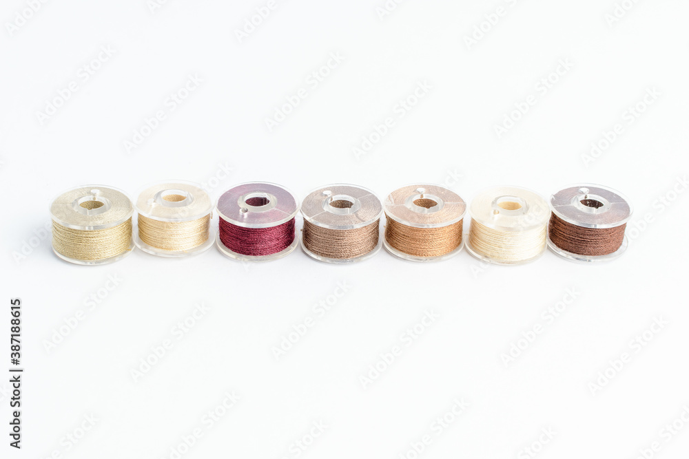Different spools of mixed beige and brown cotton thread prepared for sewing machine, isolated on white, side view. Different spools of mixed beige and brown cotton thread prepared for sewing machine, isolated on white, side view.