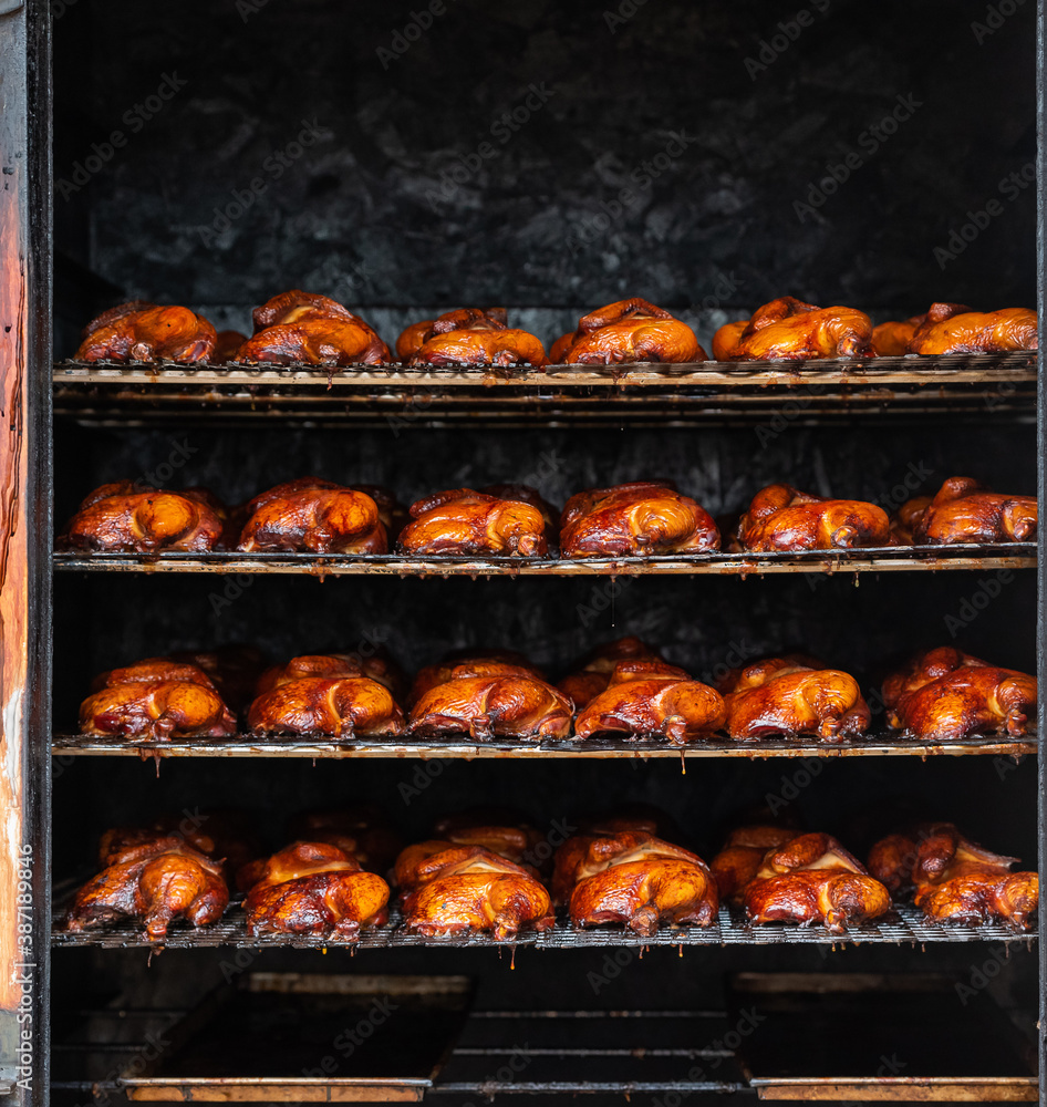 Smoke house chicken. Meat being roasted and cooked in a large smoker. Four racks of half chickens. 