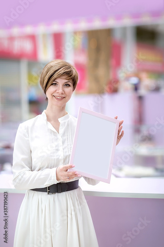 A beautiful young woman stands in a shopping center (or restaurant), holding a frame for ads. photo
