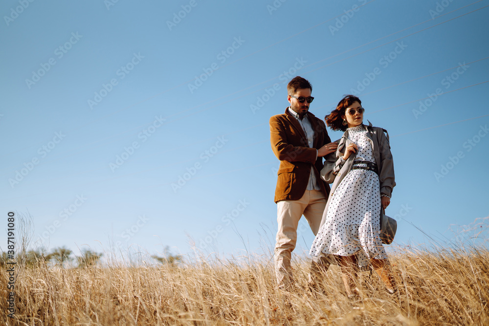 Stylish young couple enjoying autumn weather in autumn field. Lovely couple walking and hugging in the field together. The concept of youth, love and lifestyle. Stylish young couple enjoying autumn weather in autumn field. Lovely couple walking and hugging in the field together. The concept of youth, love and lifestyle.