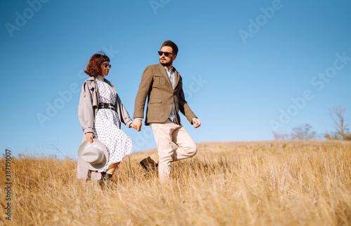 Stylish  young couple enjoying autumn weather in autumn field. Lovely couple walking and hugging in the field together. The concept of youth, love and lifestyle.