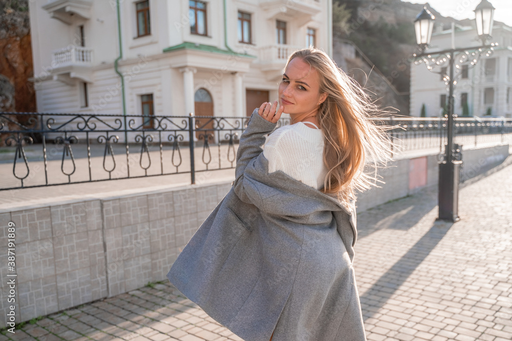 Outdoor photo of a romantic European blonde woman with long hair spending time outdoors exploring a European city. A graceful young lady in a grey coat enjoys the view of the embankment. Outdoor photo of a romantic European blonde woman with long hair spending time outdoors exploring a European city. A graceful young lady in a grey coat enjoys the view of the embankment.