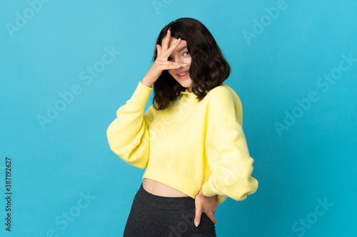 Teenager Ukrainian girl isolated on blue background covering eyes by hands and smiling © luismolinero