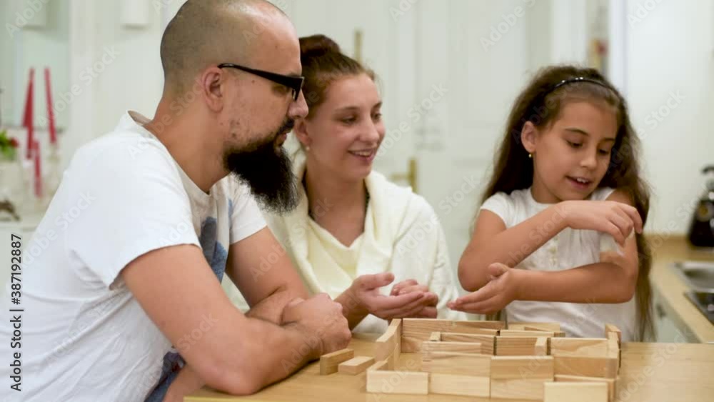Mom and dad with a little daughter playing with a hamster. Happy family kids little girl play in wooden blocks cubes build house. Mom and dad with a little daughter playing with a hamster. Happy family kids little girl play in wooden blocks cubes build house.