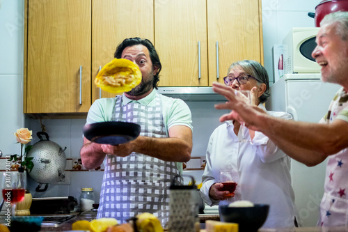 Funny family in the kitchen cooking eggs and jumping them - surprised and fun expressions from senior mother and father while adult son jump the food