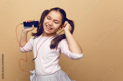 Pretty little girl listening musin on her headphones, with closed eyes, posing in studio, on beige background.