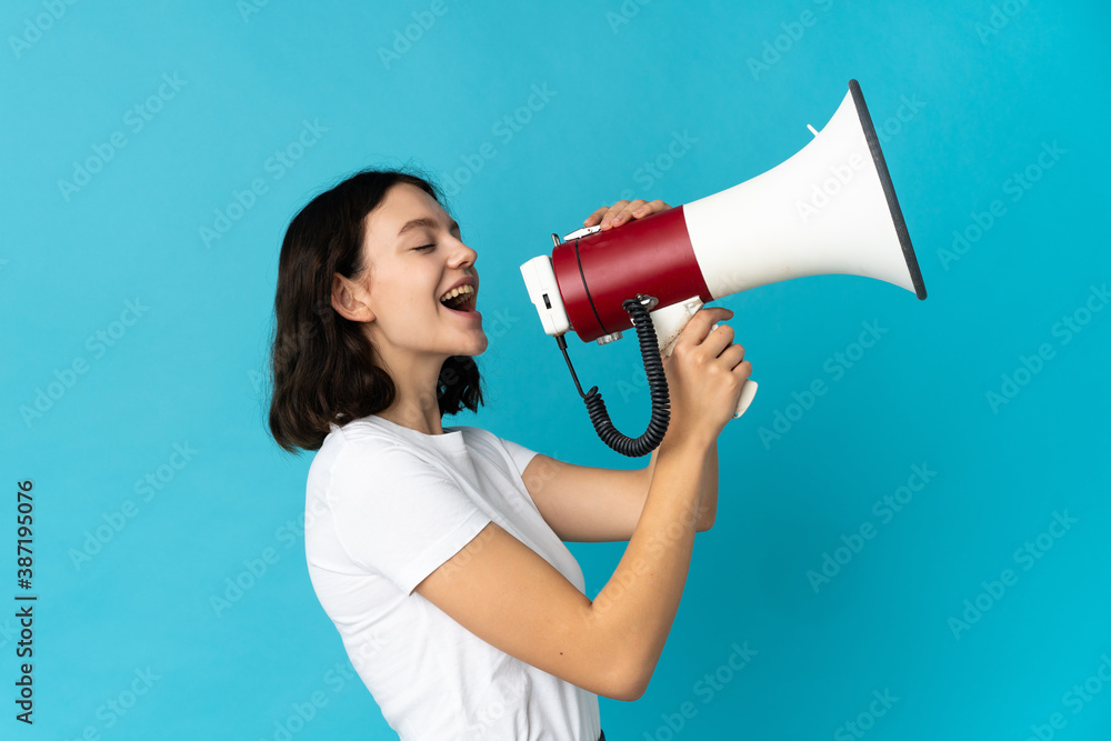 Teenager Ukrainian girl isolated on white background shouting through a megaphone to announce something in lateral position Teenager Ukrainian girl isolated on white background shouting through a megaphone to announce something in lateral position