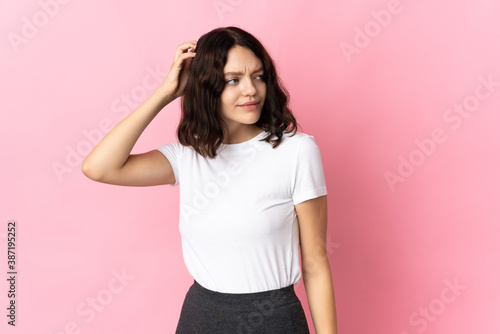 Teenager Ukrainian girl isolated on pink background having doubts while scratching head
