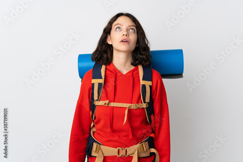 Teenager mountaineer girl with a big backpack isolated on white background looking up and with surprised expression