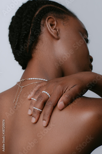 African woman turned naked back in studio on white background. Dark-skinned model hugs herself with her hands with rings on her fingers