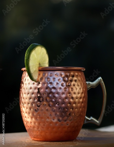 Cocktail mule cup also called a copper mug containing Moscow mule vodka cocktail, garnished with a lime slice, isolated on a wooden surface © Nodi