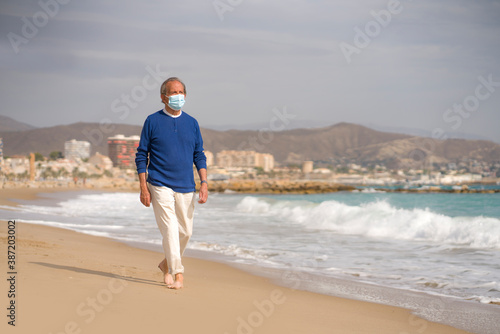 Senior pensioner relaxed in beach during new normal - retired old man on his 70s wearing surgical mask against covid19 walking at the sea thoughtful and contemplative