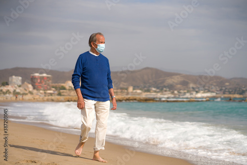 Senior pensioner relaxed in beach during new normal - retired old man on his 70s wearing surgical mask against covid19 walking at the sea thoughtful and contemplative © TheVisualsYouNeed