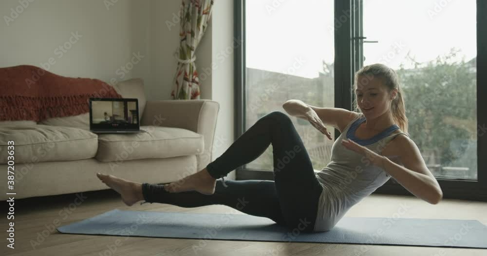 Female practicing pilates exercise at home watching video tutorial on laptop Female practicing pilates exercise at home watching video tutorial on laptop