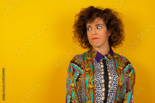 Photo of amazed puzzled young Caucasian female with ginger hair knot, curves lips and has worried look, sees something awful in front, isolated on white background, dressed in jean overalls.