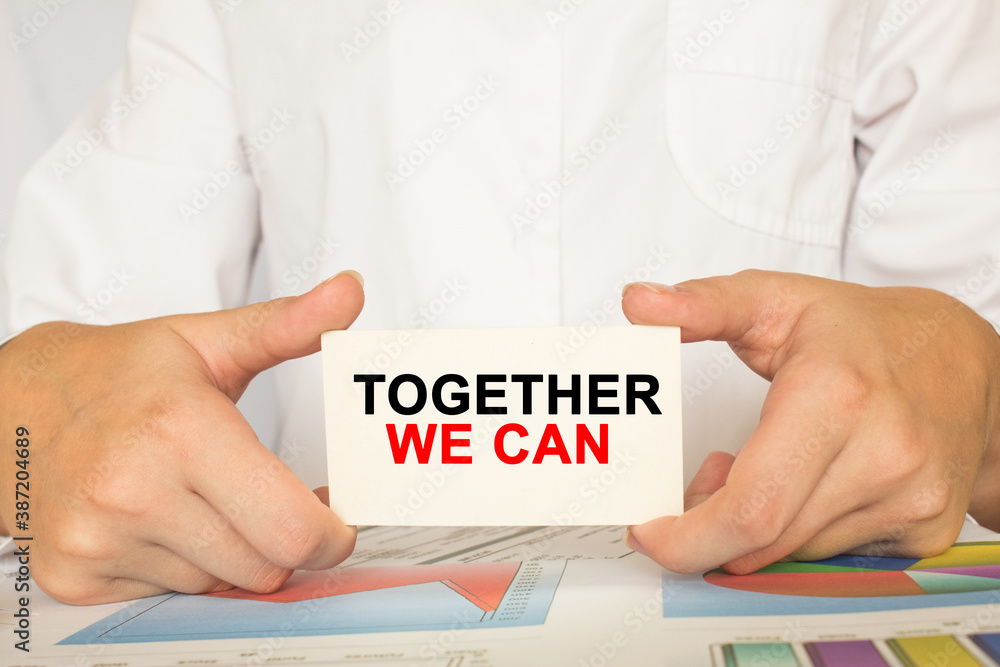 a man in the office holds a card with text TOGETHER WE CAN. business concept a man in the office holds a card with text TOGETHER WE CAN. business concept
