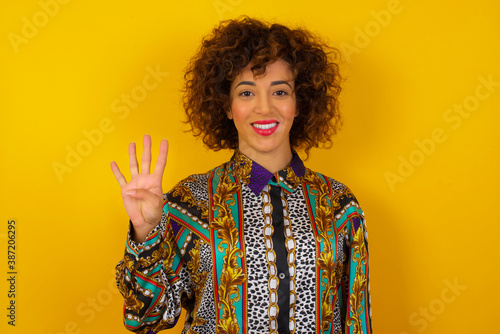 Young woman standing against gray wall showing and pointing up with fingers number four while smiling confident and happy.