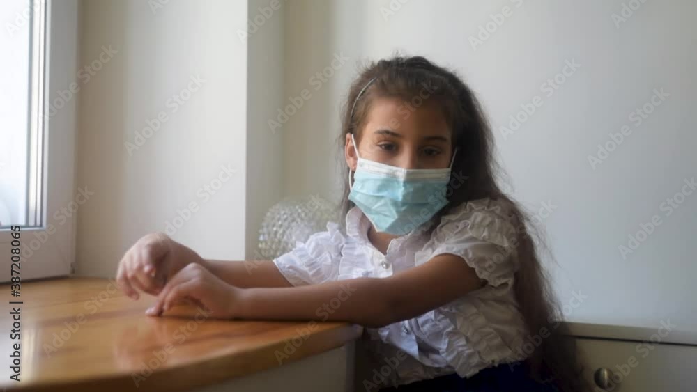 Little girl on home quarantine. Protective medical mask. Girl stand in front of window glass. Wave hands. Covid-19 coronavirus pandemic, prevention epidemic. Stay home. Little girl on home quarantine. Protective medical mask. Girl stand in front of window glass. Wave hands. Covid-19 coronavirus pandemic, prevention epidemic. Stay home.