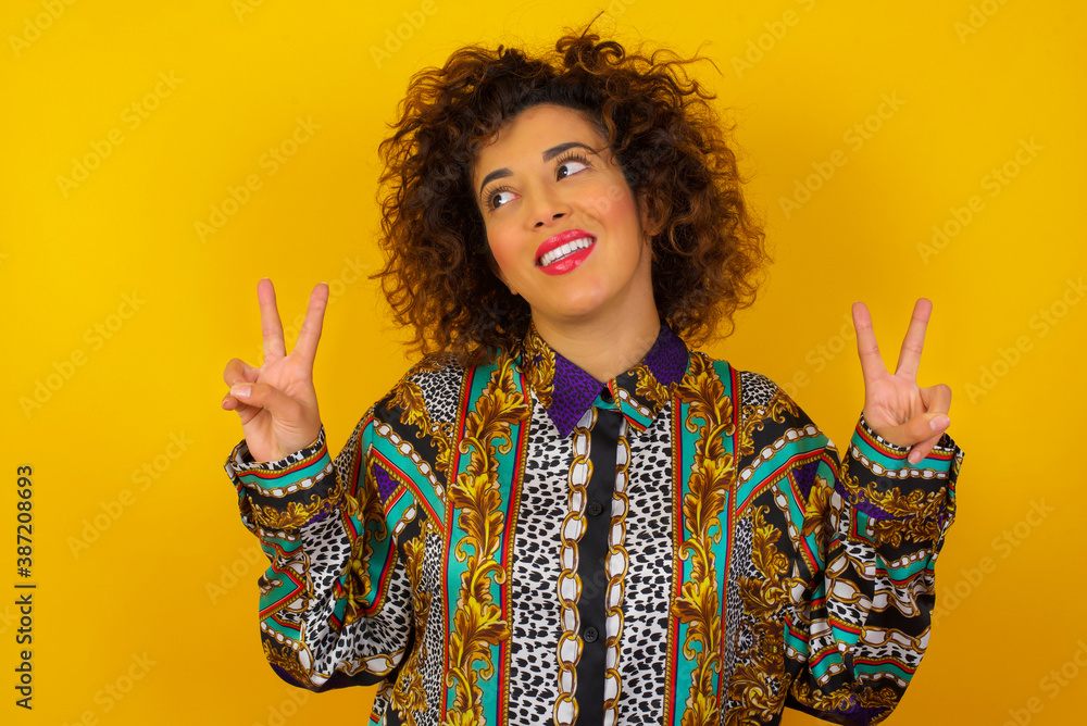 Isolated shot of cheerful woman makes peace or victory sign with both hands, dressed in casual clothes, feels cool has toothy smile, isolated over gray background. People and body language. Isolated shot of cheerful woman makes peace or victory sign with both hands, dressed in casual clothes, feels cool has toothy smile, isolated over gray background. People and body language.