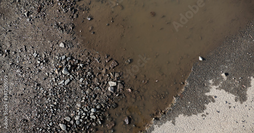 A brown puddle on an old village road, water and asphalt