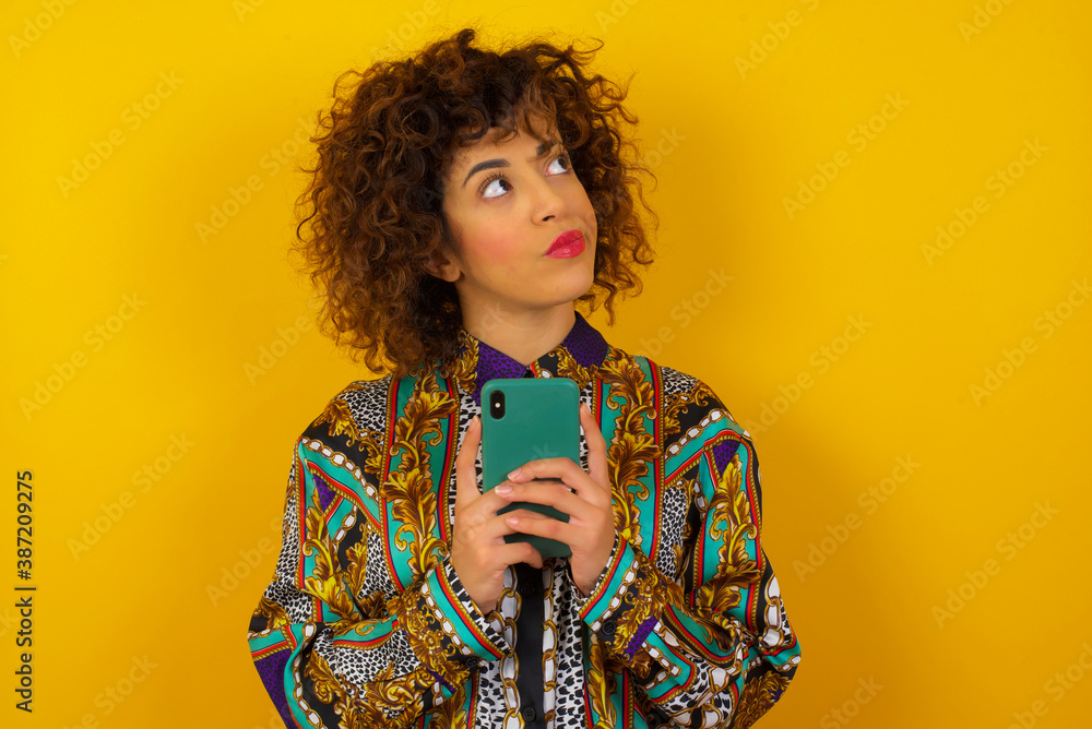 Portrait of beautiful young woman with dreamy look, thinking while holding smartphone, isolated over white background. Tries to write up a message for her father, explaining why she took car Portrait of beautiful young woman with dreamy look, thinking while holding smartphone, isolated over white background. Tries to write up a message for her father, explaining why she took car