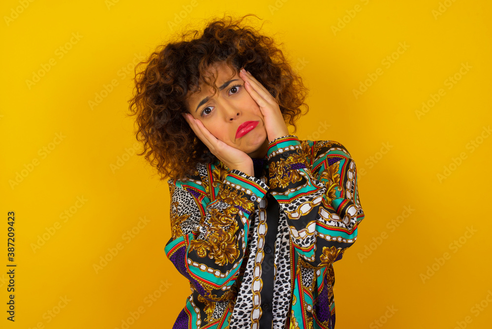 Portrait of beautiful young woman holding head in hands with unhappy expression watching sad movie about animals and trying not to cry.