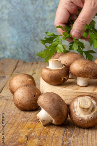Close-up of portobello mushrooms and woman's hand holding parsley, on rustic wooden table and gray background, vertical photo