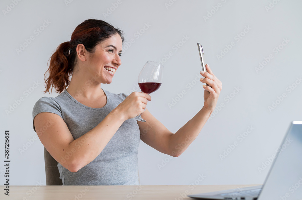 Caucasian woman drinks red wine and communicates with friends via video communication on a smartphone. The quarantined girl celebrates the holiday via an online conference Caucasian woman drinks red wine and communicates with friends via video communication on a smartphone. The quarantined girl celebrates the holiday via an online conference