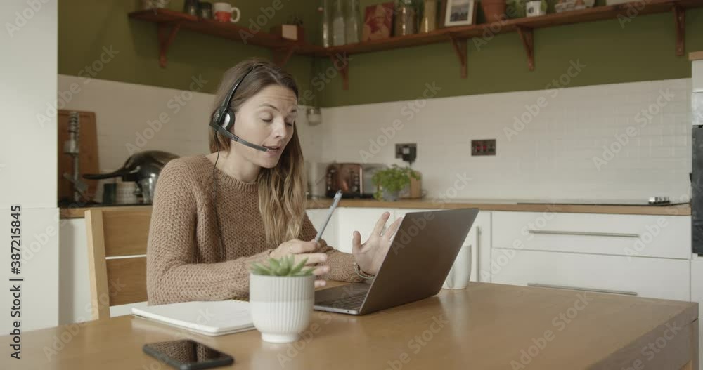 Female using headset during video call, working from home at kitchen table during pandemic