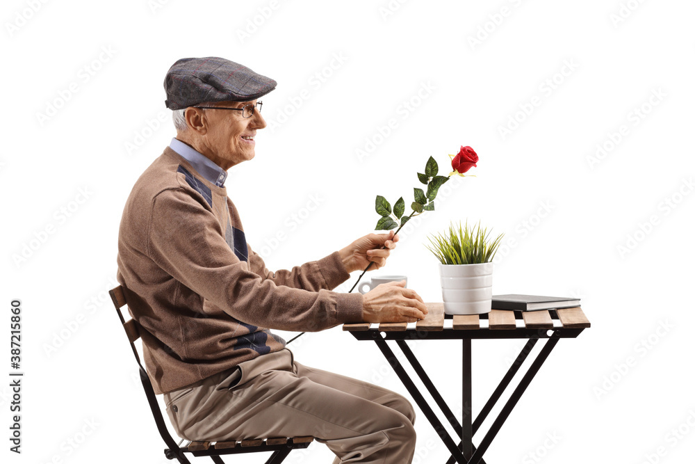 Elderly man sitting at a coffee table alone and holding a red Elderly man sitting at a coffee table alone and holding a red