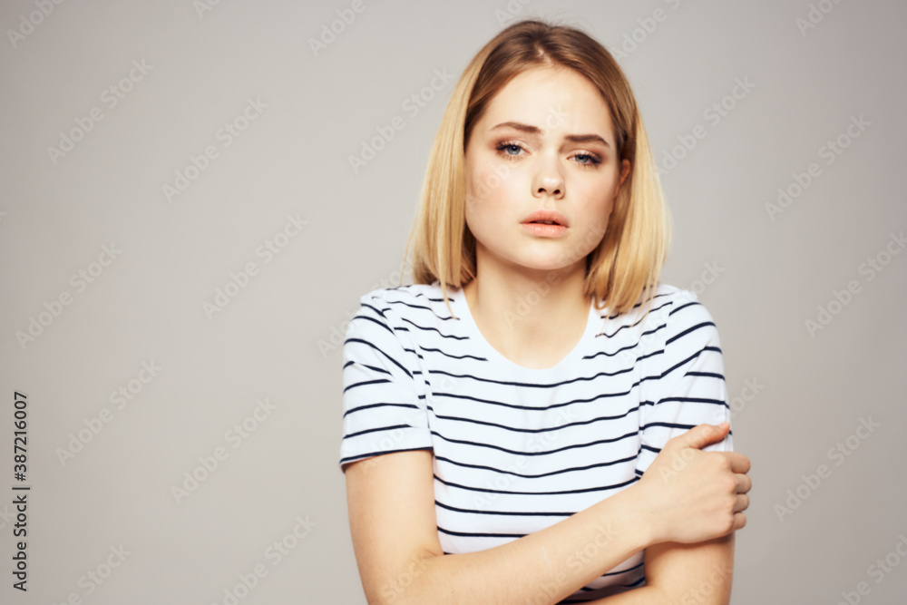 A woman in a striped T-shirt holds her hands in front of her emotions displeasure light background A woman in a striped T-shirt holds her hands in front of her emotions displeasure light background