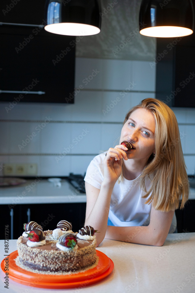 Young woman baked a cake. Girl tastes chocolate covered strawberries