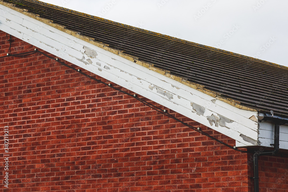 Flaking paint on wooden fascia boards to a side of a brick built building ภาพถ่ายสต็อก Adobe Stock